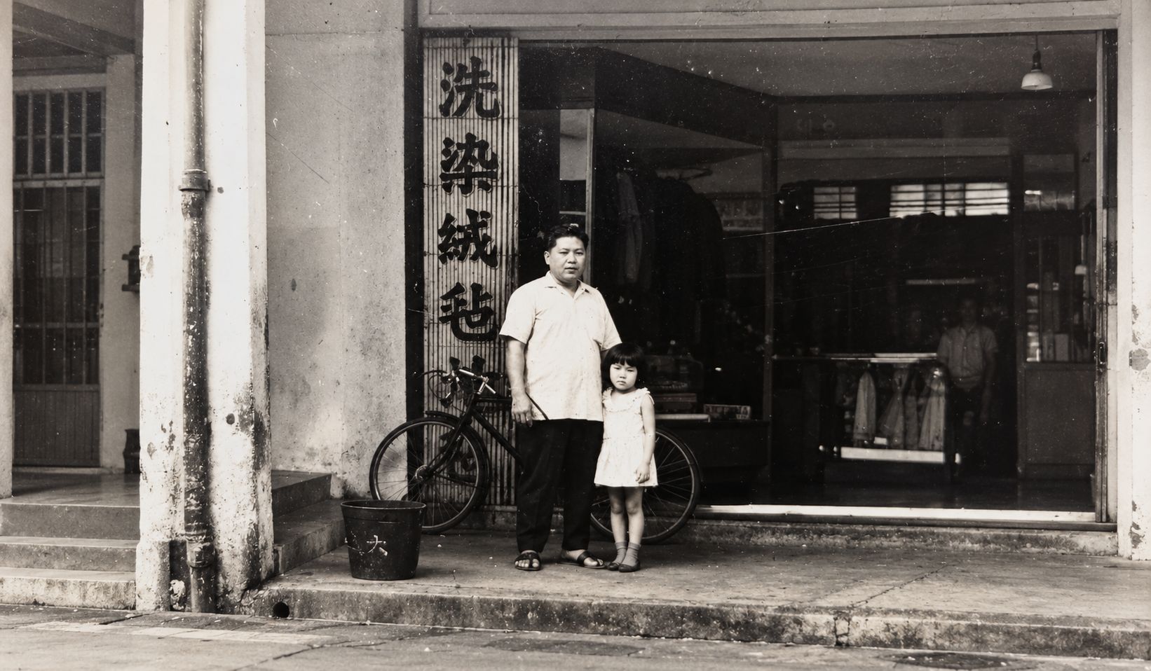 Archival photo of the family's early laundry shopfront, with the founder and his daughter standing outside